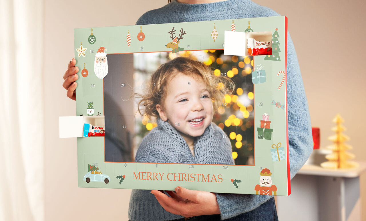 Un copil ține un cadru foto festiv cu inscripția „MERRY CHRISTMAS”. Lumini de Crăciun strălucesc în spate.