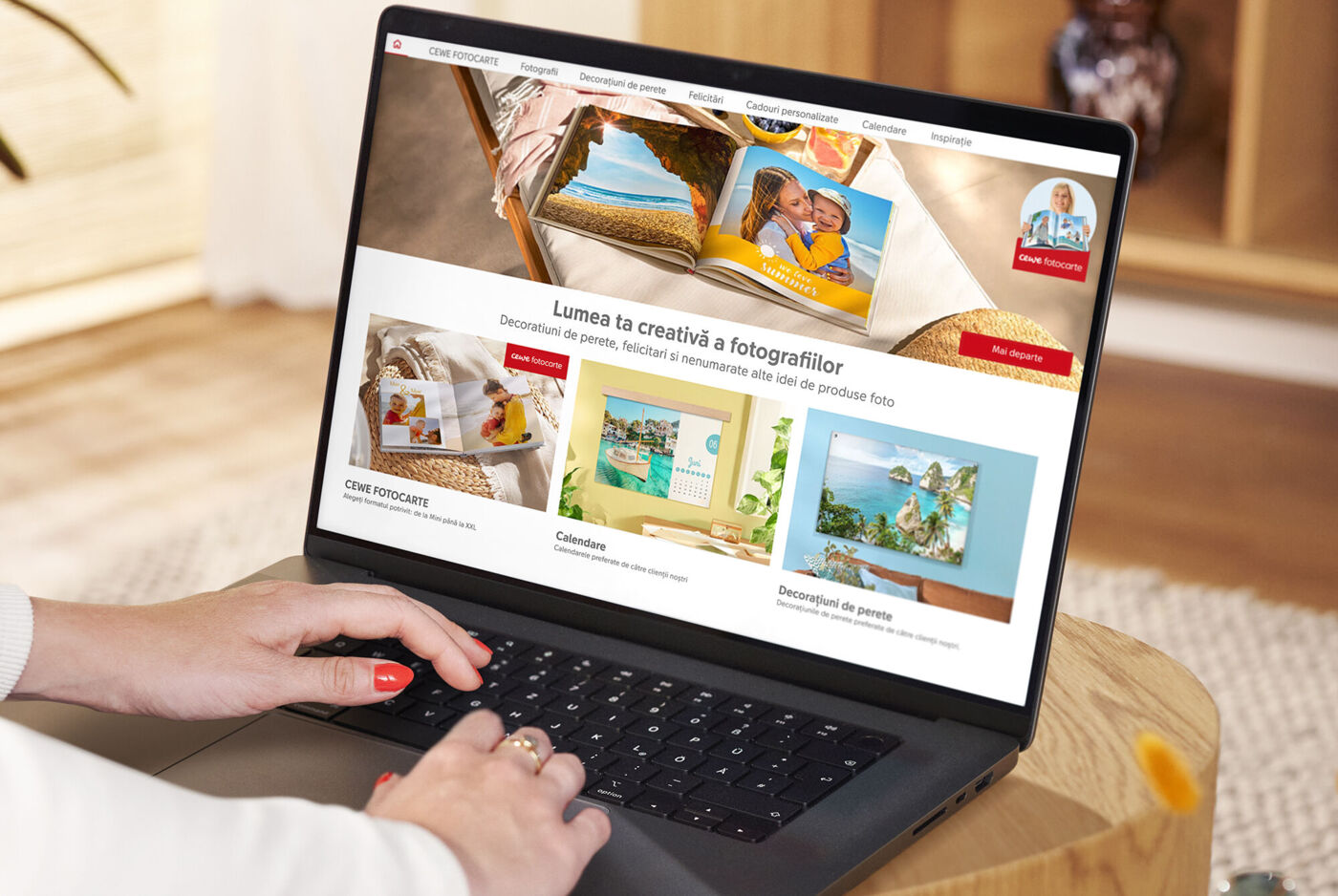 Persoană lucrând la laptop creând o pagină CARTE FOTO CEWE, atmosferă veselă cu plante în fundal.