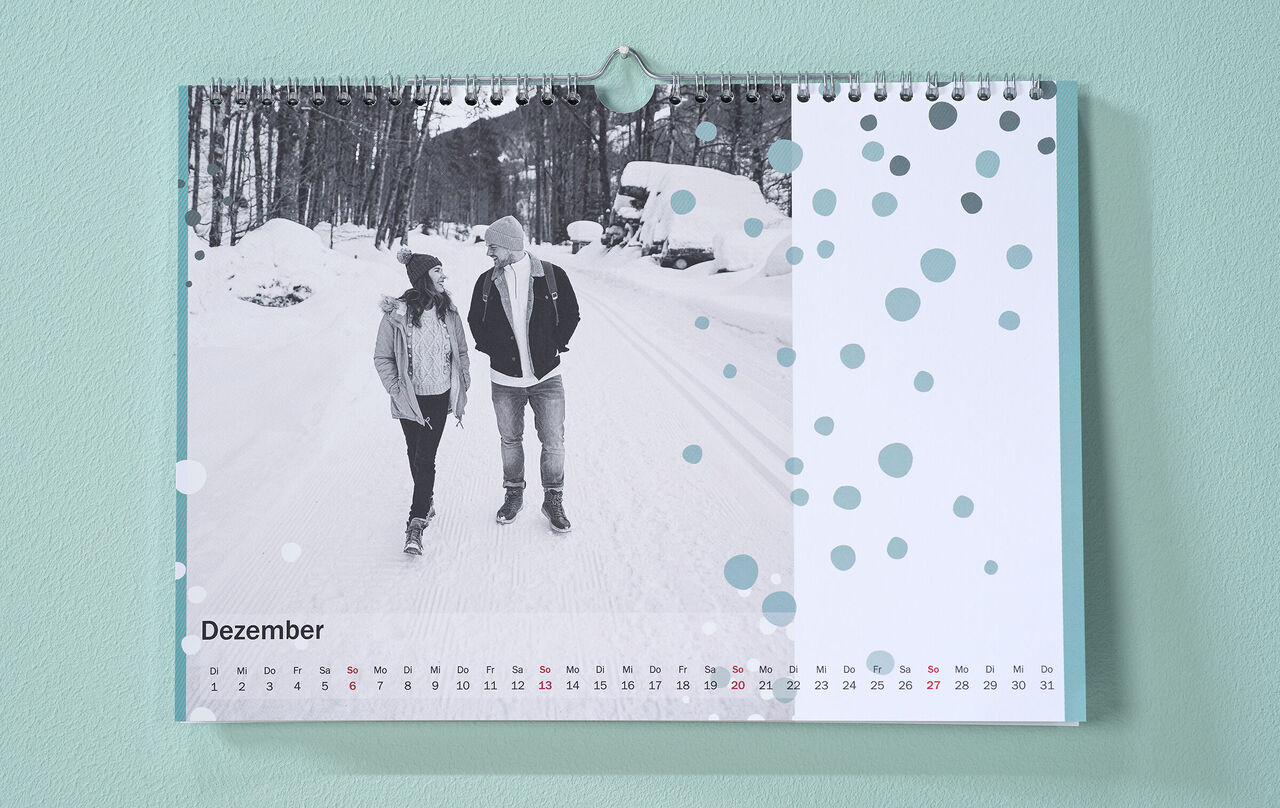 Pe perete este agățat un calendar cu tematică de iarnă, cu o fotografie a unui cuplu și un clipart cu buline.